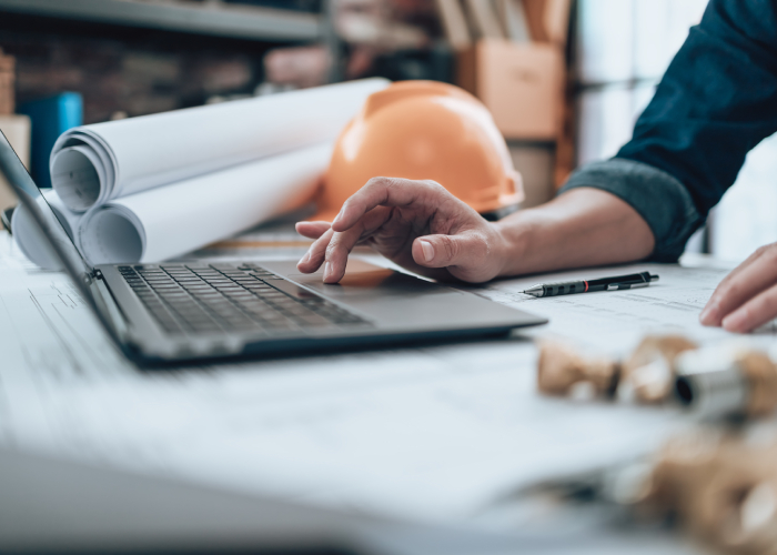 Engineer working on a laptop with blueprints and tools, symbolizing technology and innovation driving project management trends