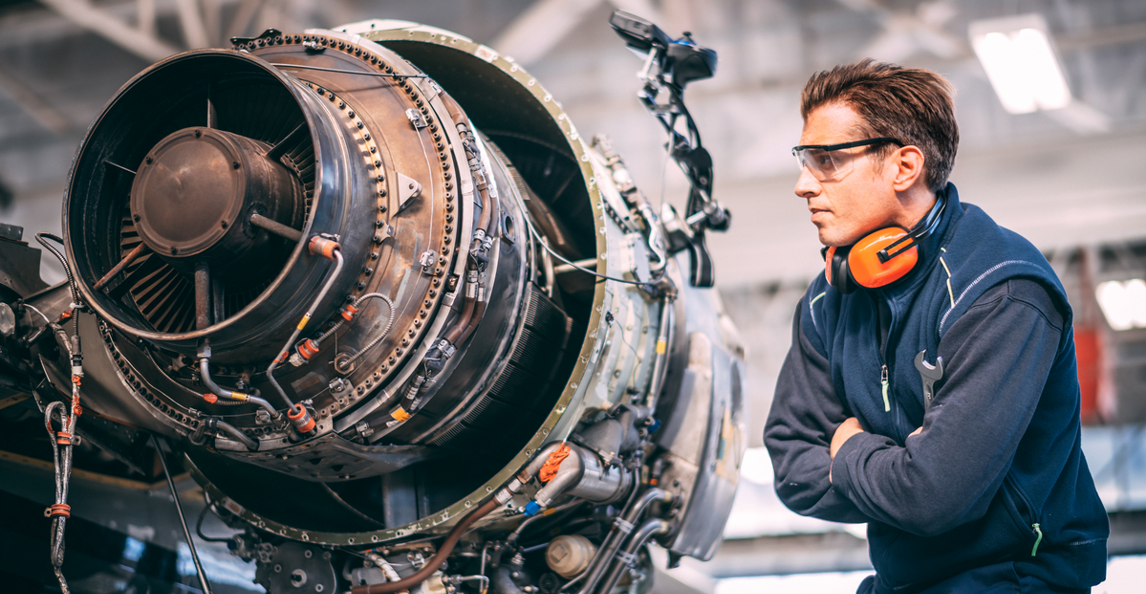 Aerospace technician in safety glasses inspecting a jet engine in a hangar
