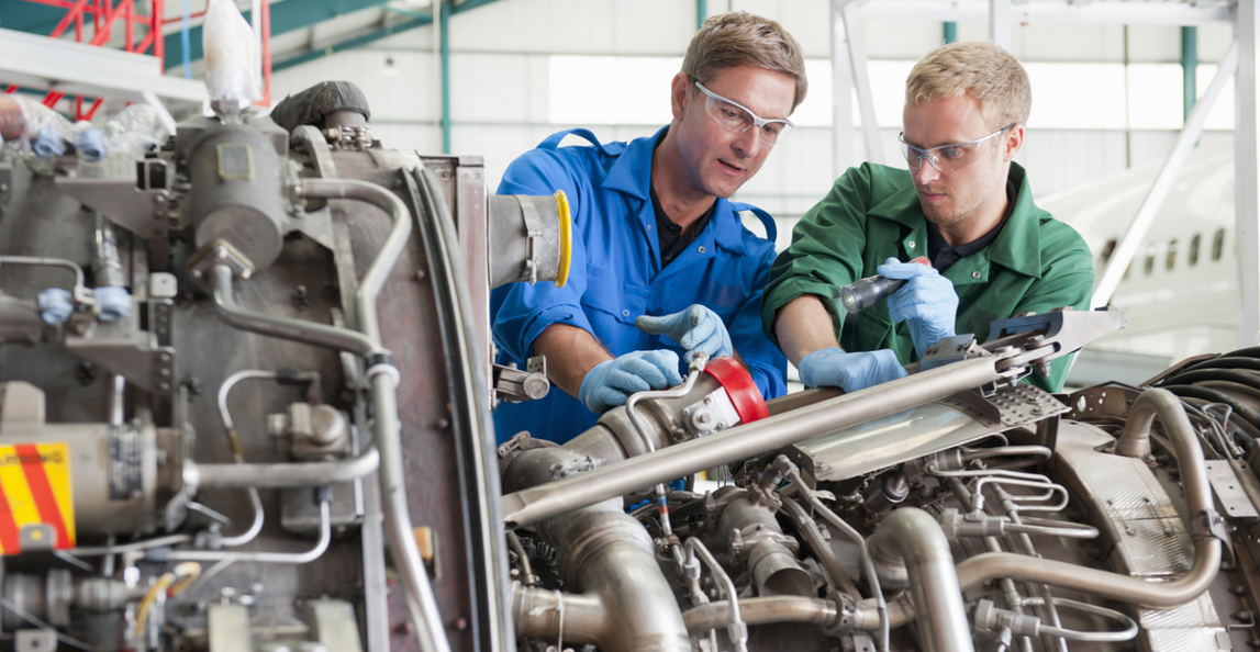 Two aerospace technicians in safety glasses performing aircraft engine maintenance in a hangar