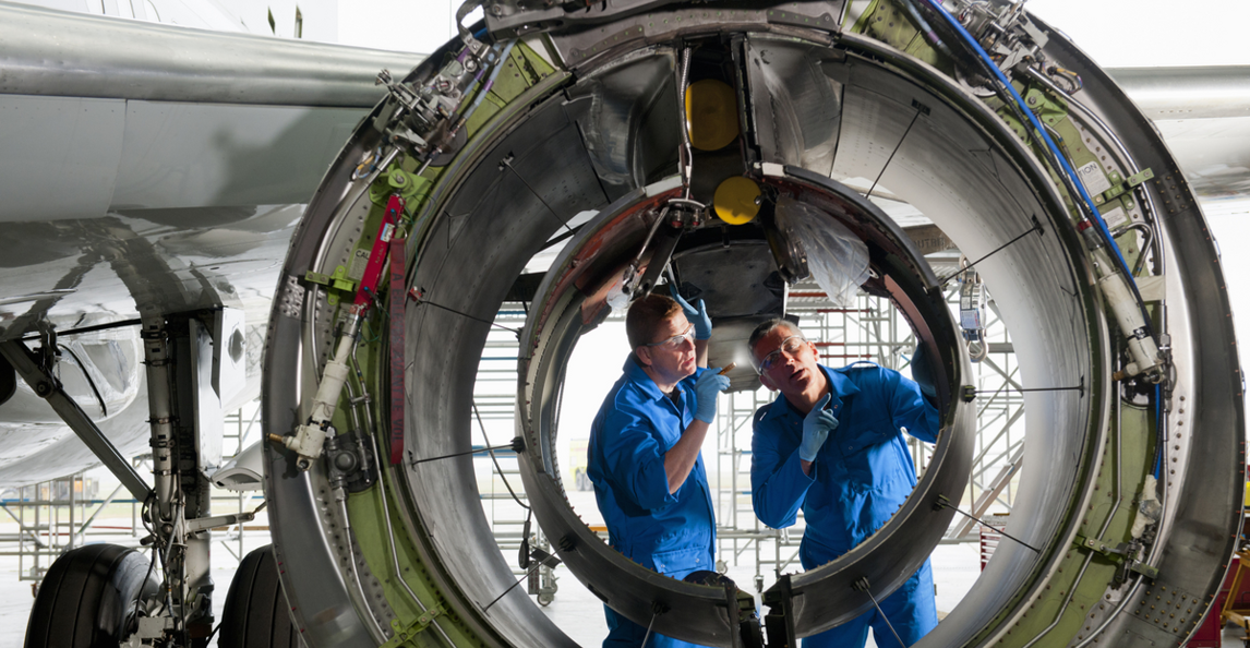 Two aerospace technicians performing aircraft engine maintenance and inspection in a hangar