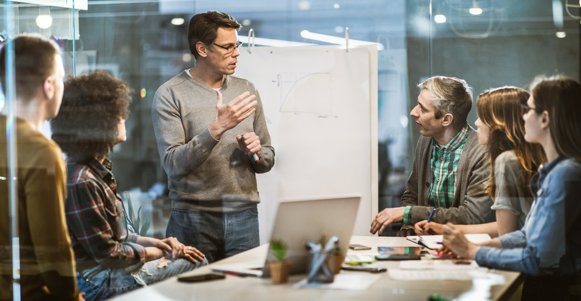 Business leader presenting a strategy to a team in a modern glass-walled meeting room