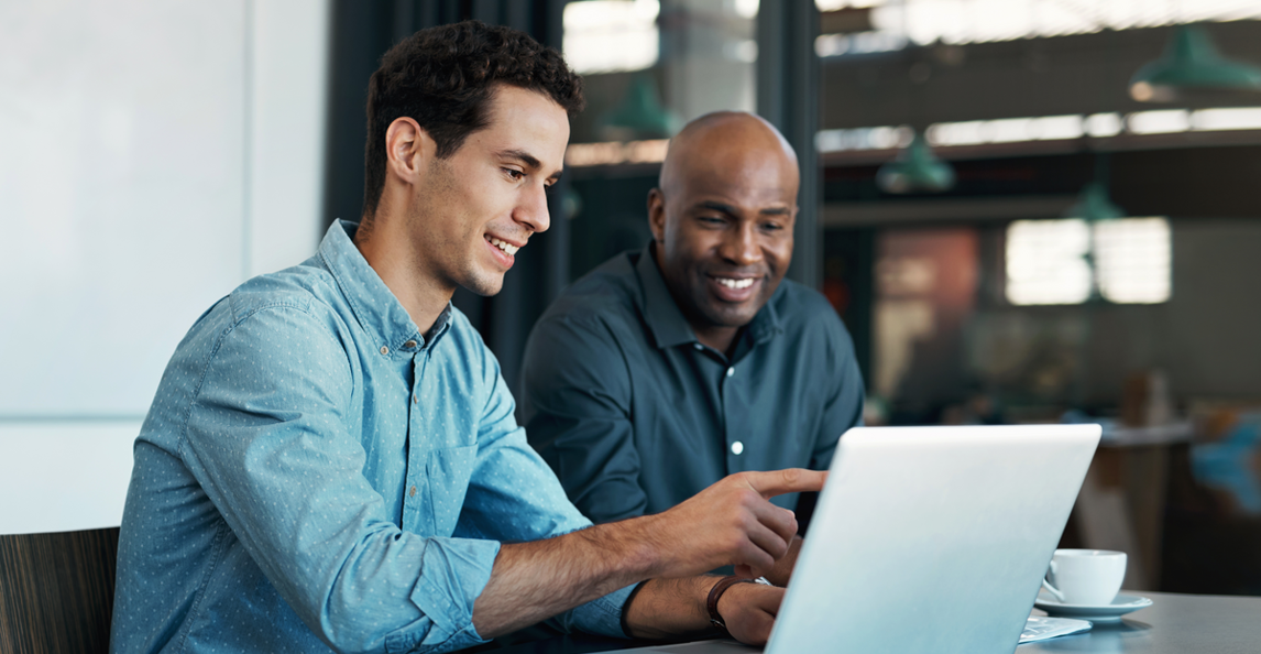 Two business professionals smiling while reviewing financial data on a laptop in a modern office
