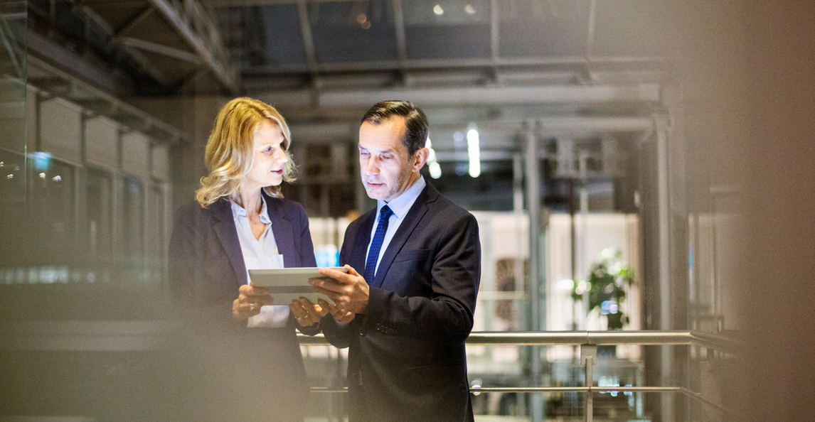 Two business professionals review automated process insights on a tablet in a modern office.