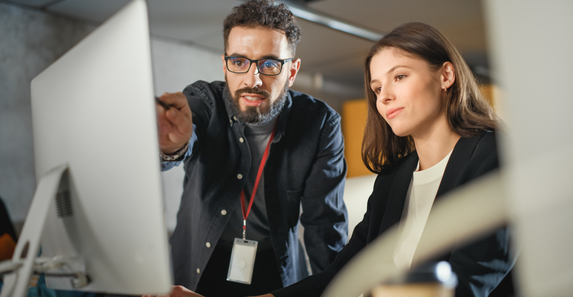 Two business professionals reviewing financial data on a desktop monitor in a modern office