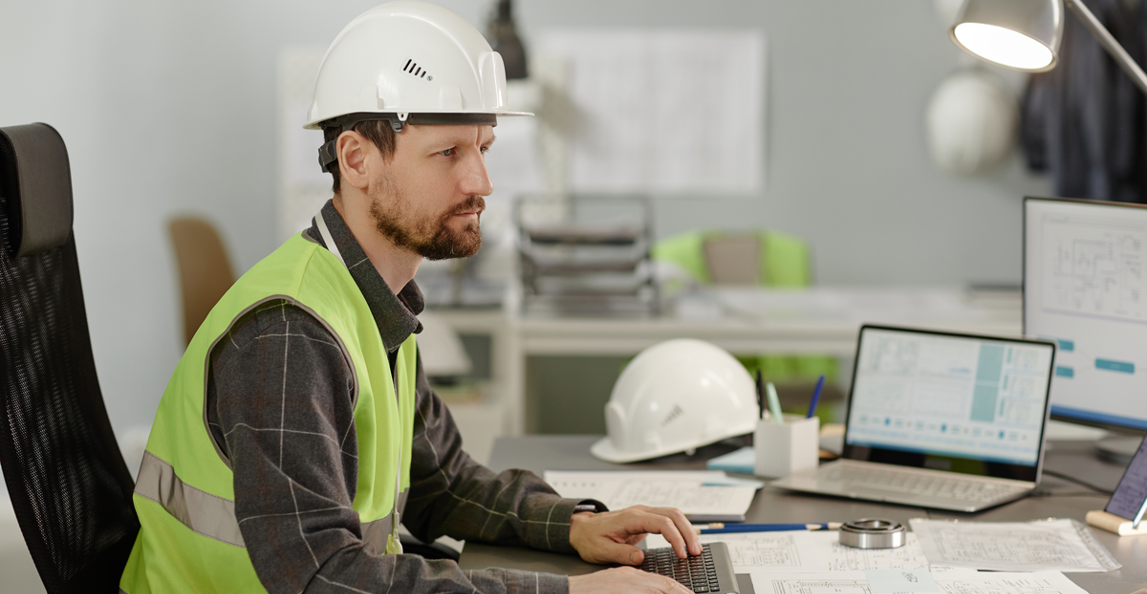 Construction billing manager reviewing project documents and software at office desk