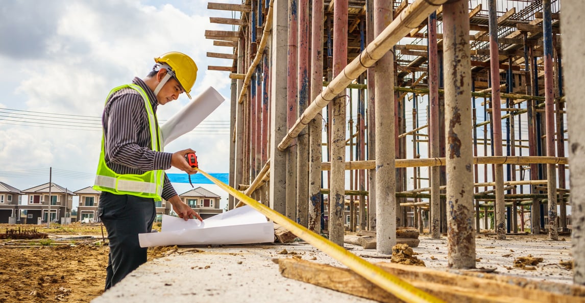 Construction engineer reviewing blueprints and measuring at a building site