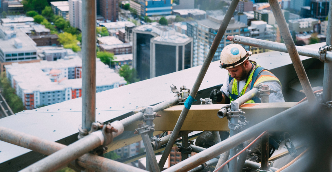 Construction worker on scaffolding working at height above a city