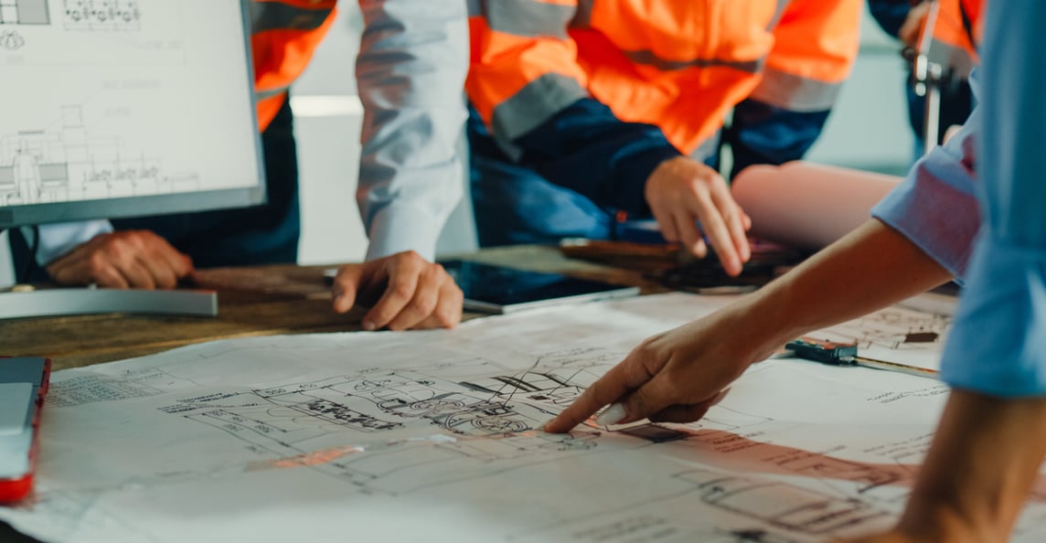 Construction professionals in hi-vis vests reviewing technical blueprints for cost estimating