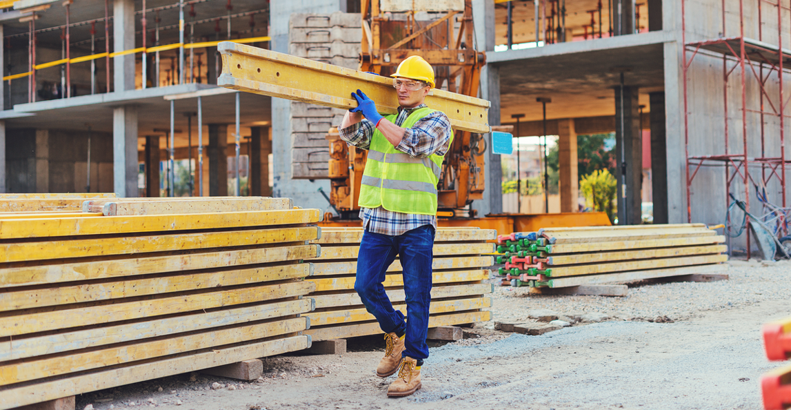 construction worker carrying planks on construction site