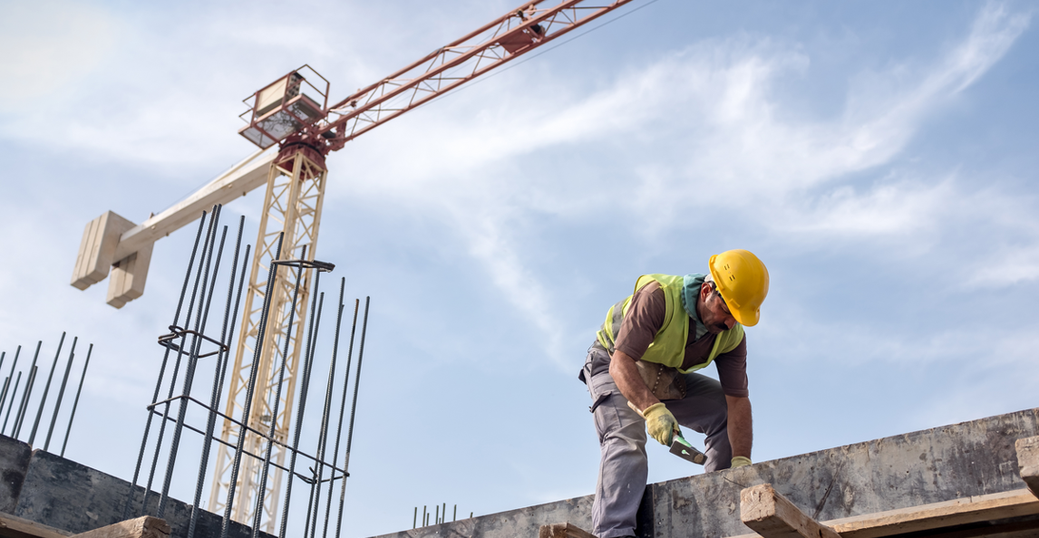 Construction worker in safety gear working at height on a building site with a crane