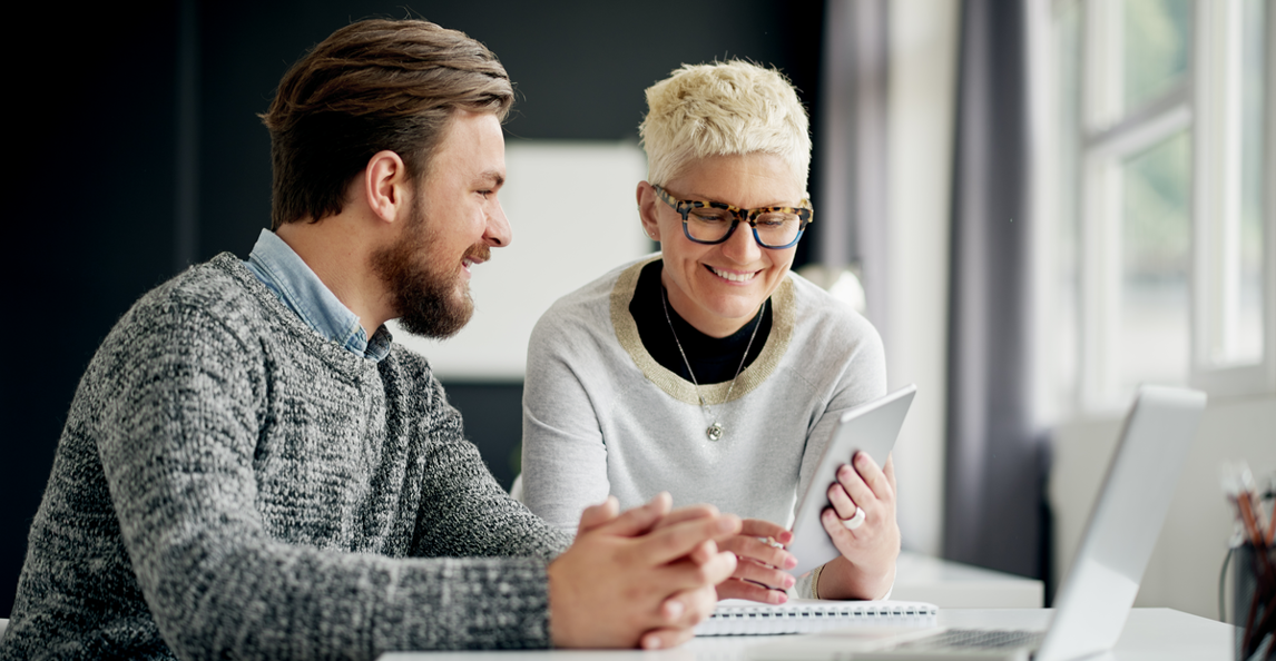 Two business professionals in a consulting meeting with one sharing content on a tablet