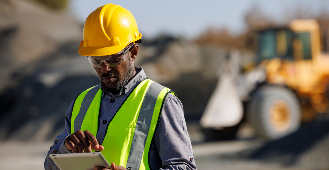 Demolition contractor using a tablet on a heavy equipment job site with a bulldozer in the background