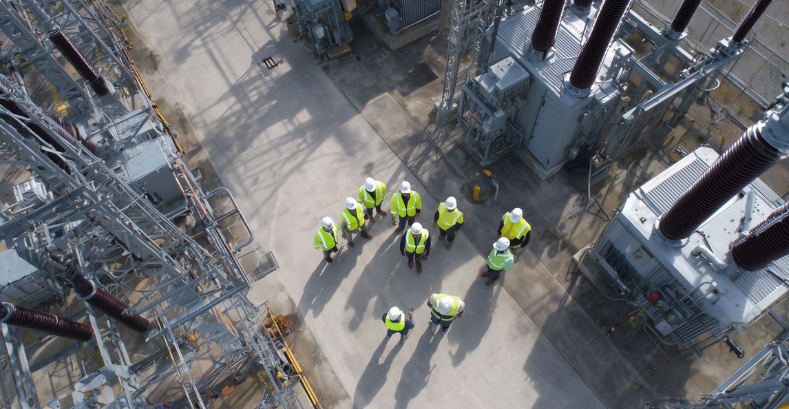 Aerial view of electrical contractors in hi-vis vests meeting at a substation