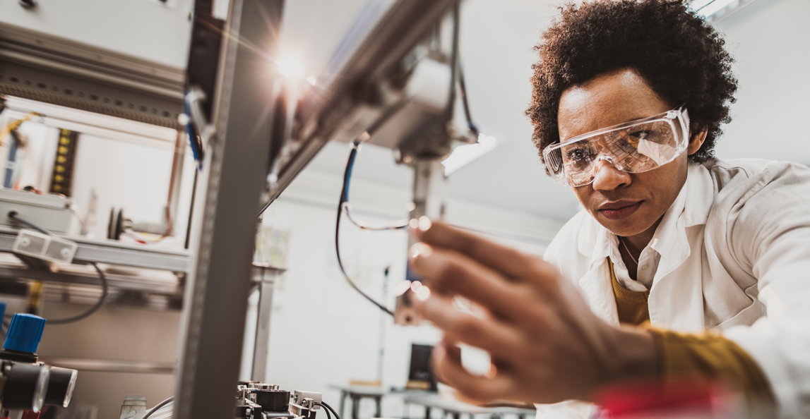 Female engineer in safety glasses carefully inspecting precision manufacturing equipment for quality and risk management