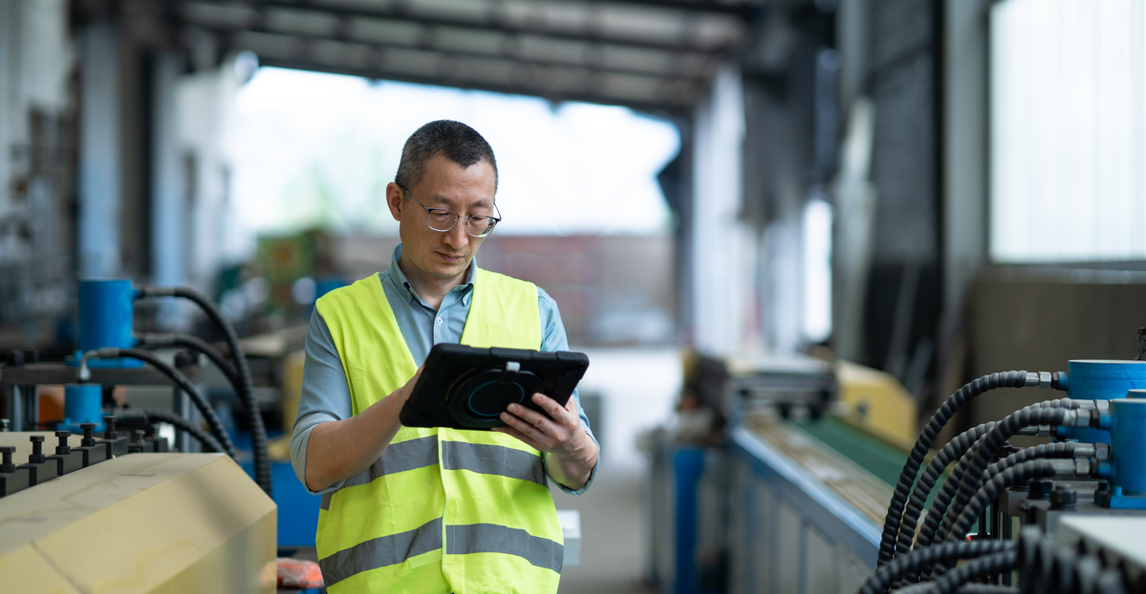 Manufacturing engineer in safety vest using a tablet on the factory floor