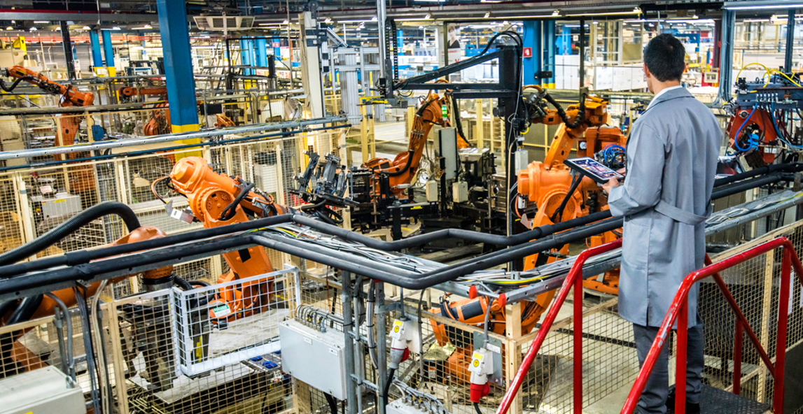 Engineer with a tablet overseeing an automated robotic production line in a factory