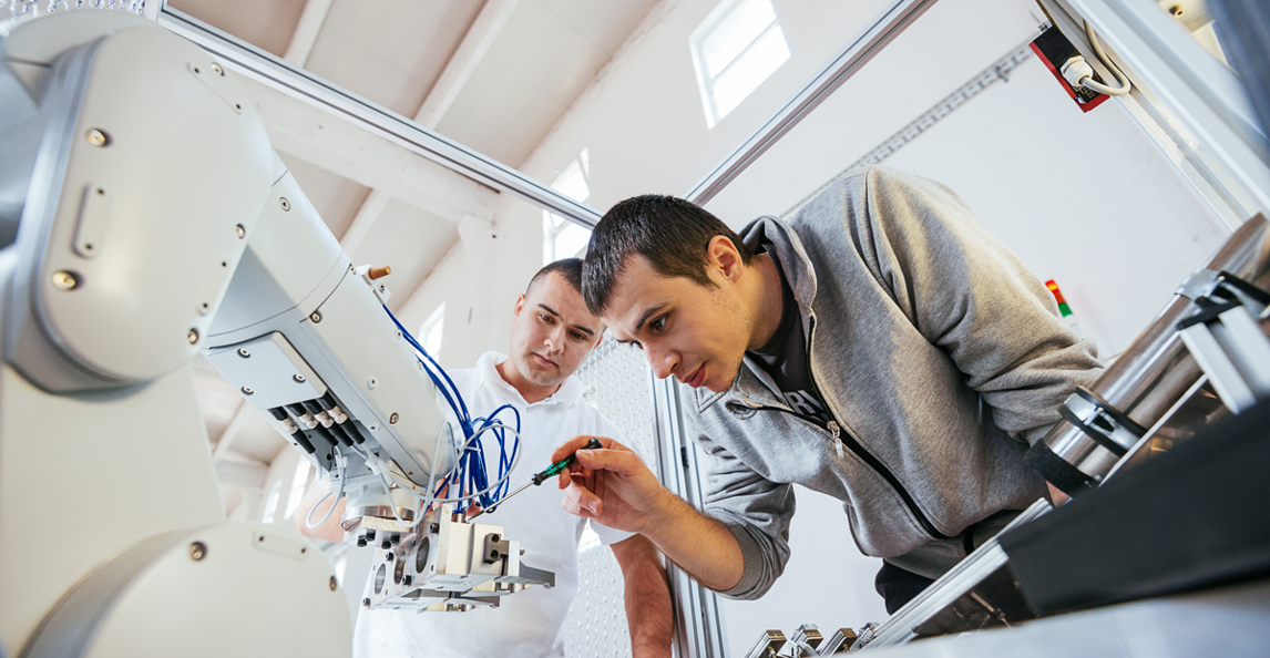 Two engineers performing precise mechanical work on a robotic arm in a factory