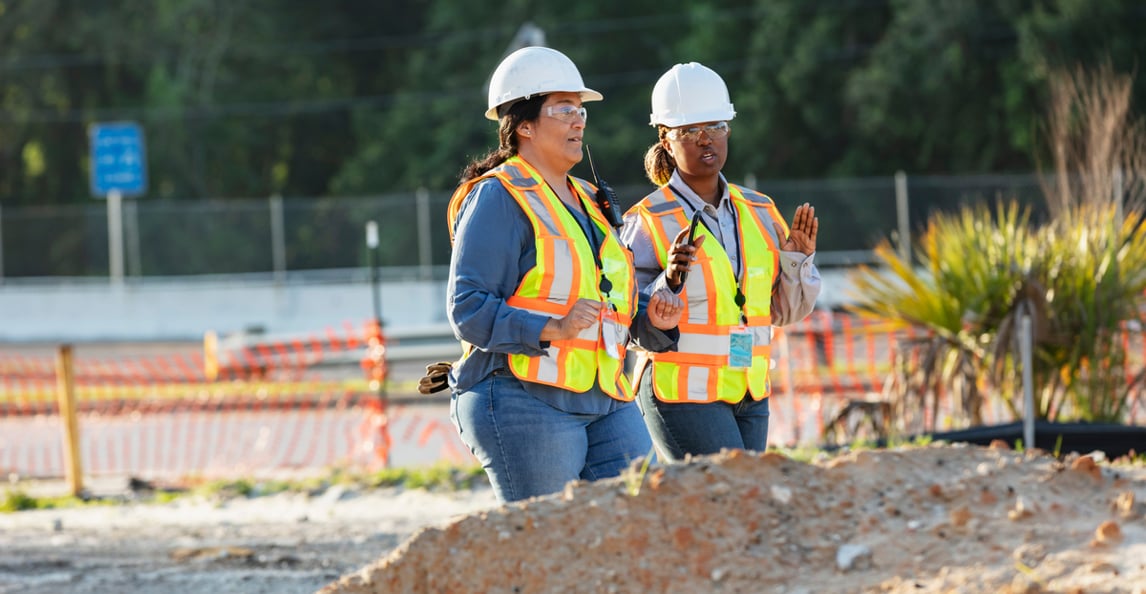 Two construction field managers in hi-vis vests supervising an active job site