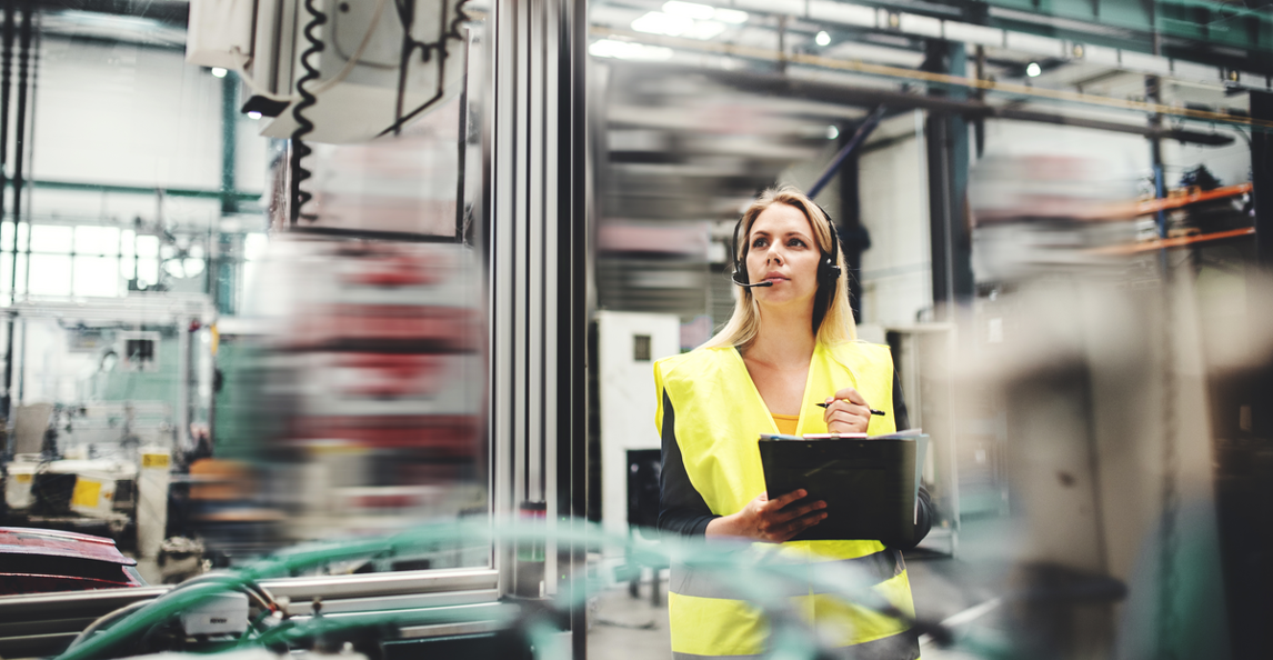 Female quality inspector with clipboard and headset monitoring a production line in a factory