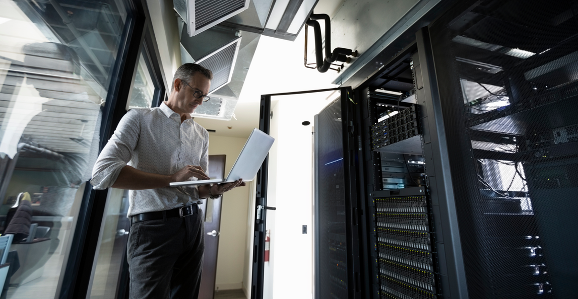 An IT professional uses a laptop in a modern server room.
