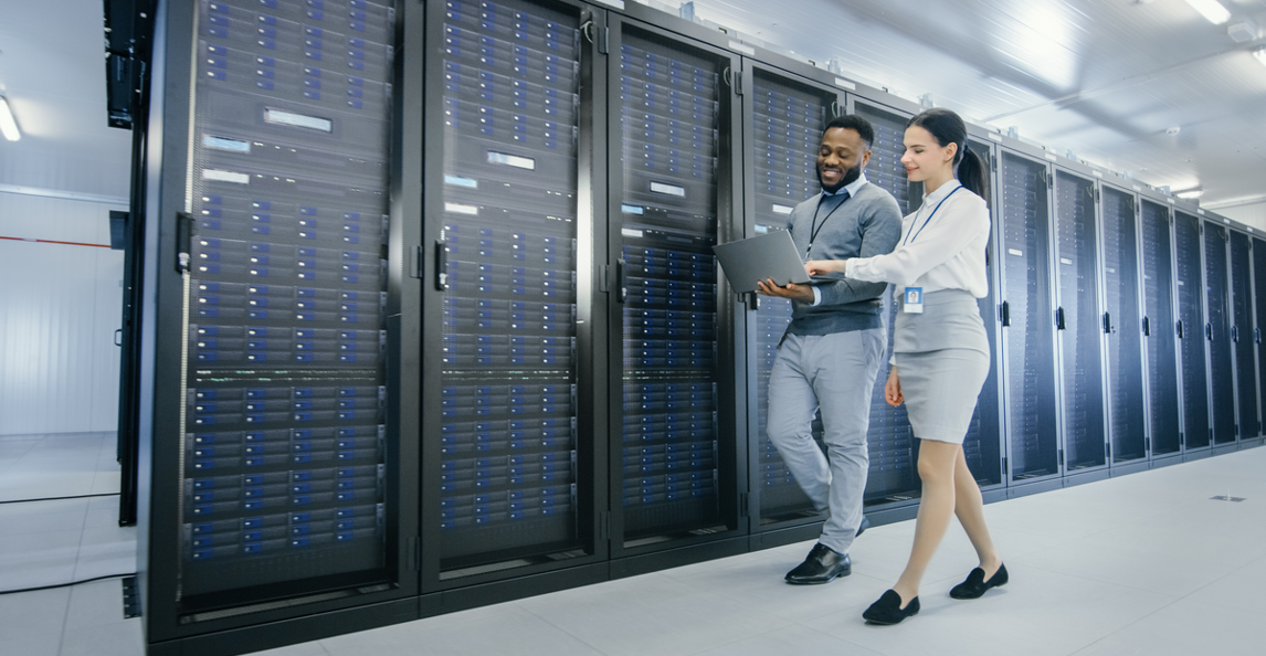 Two IT professionals reviewing a laptop while walking in a data center