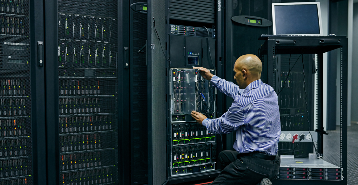 IT technician kneeling to service servers in a data center