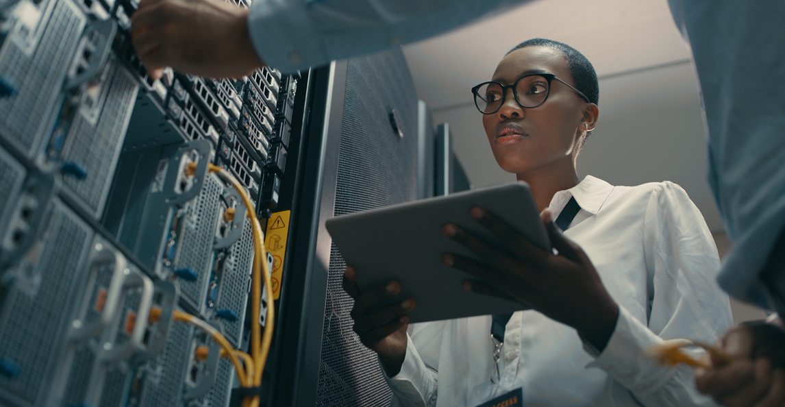 Female IT professional reviewing network infrastructure with a tablet in a server room.