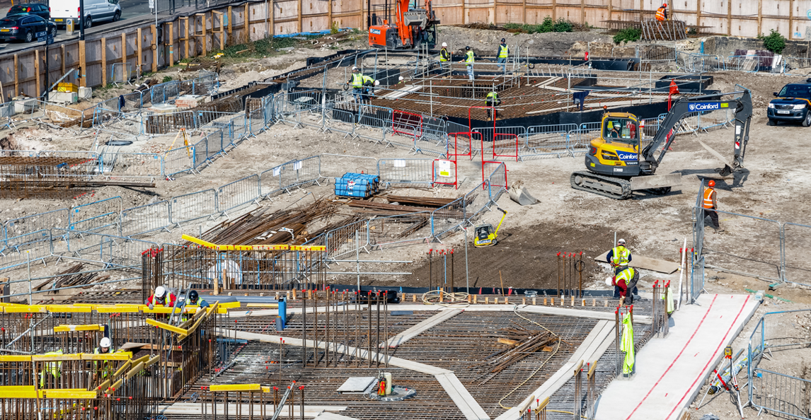 Aerial view of a large-scale construction site with workers, steel reinforcement and an excavator