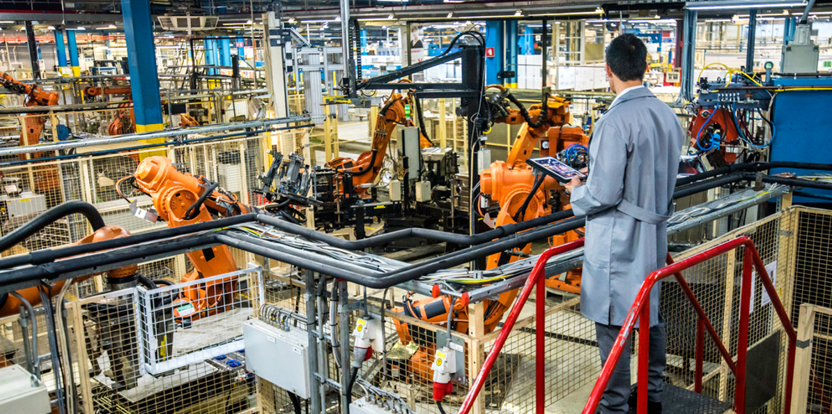 engineer monitoring automated manufacturing floor operations with a tablet to support MMAS compliance