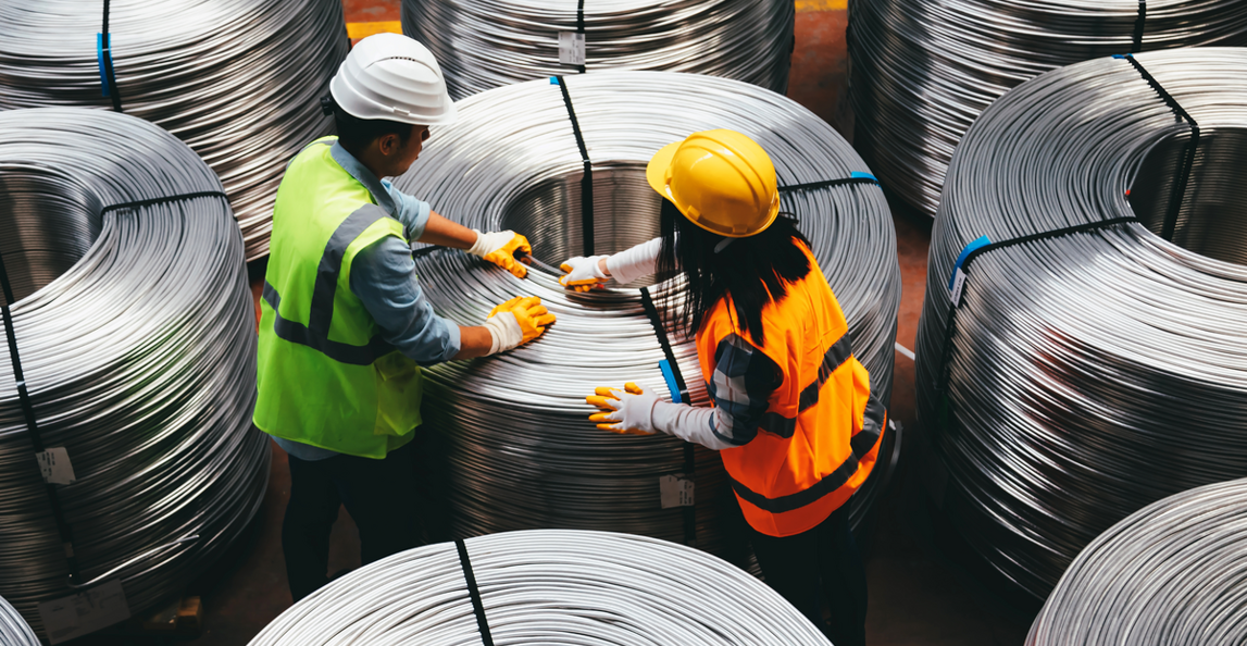 Two manufacturing workers inspecting metal wire coils in a warehouse as part of supplier quality management