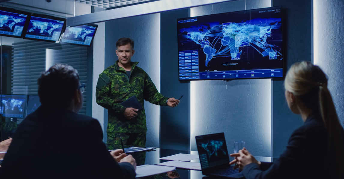 Military officer briefing a team in front of a global data display