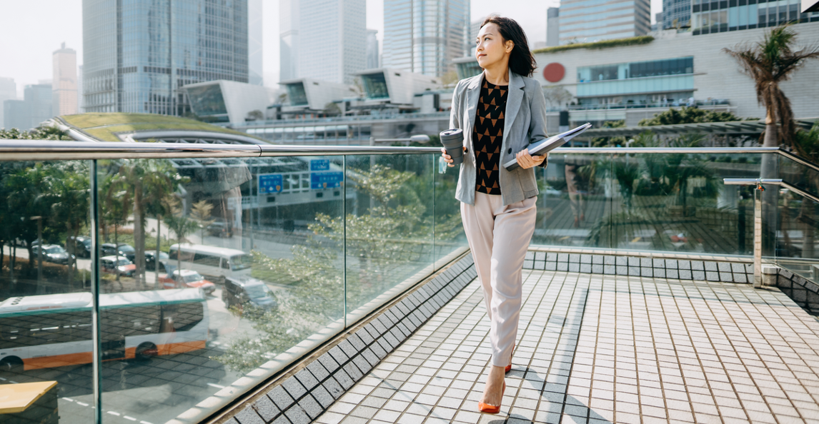 Businesswoman holding a laptop and coffee on a rooftop terrace with city skyline