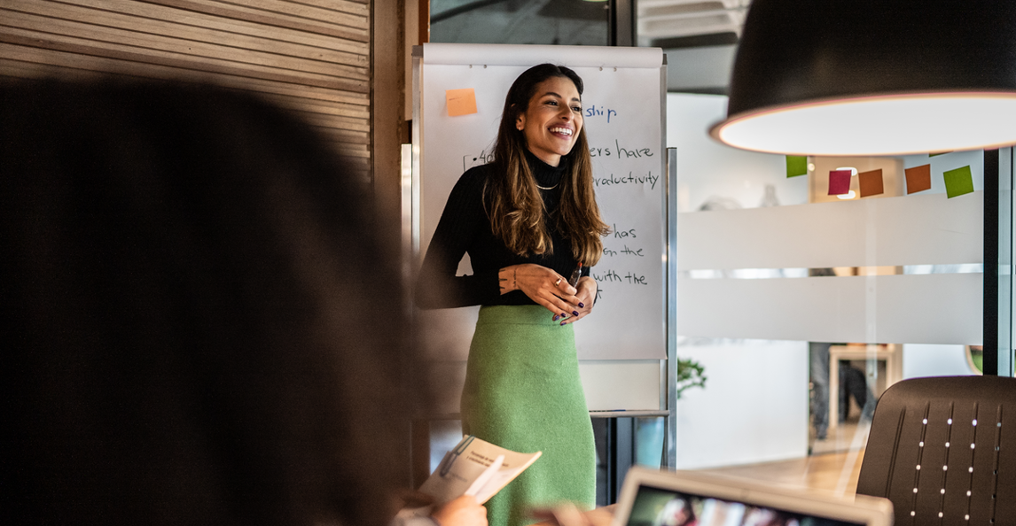 Business professional presenting to colleagues in a bright meeting room.