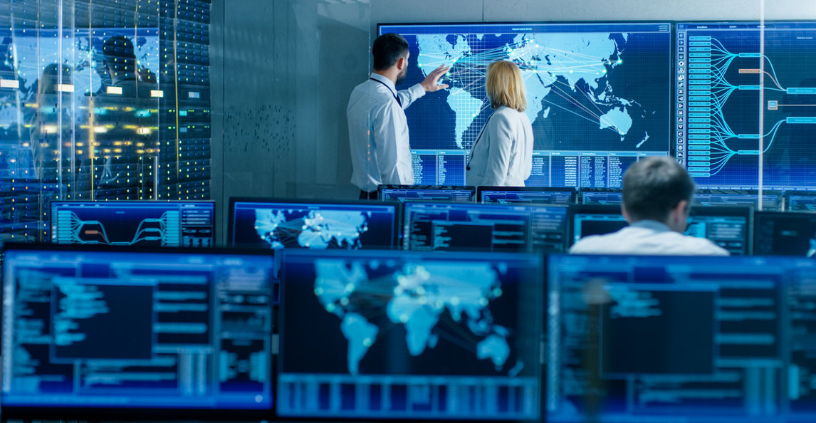Two analysts pointing at a global map on a large screen in a data monitoring room