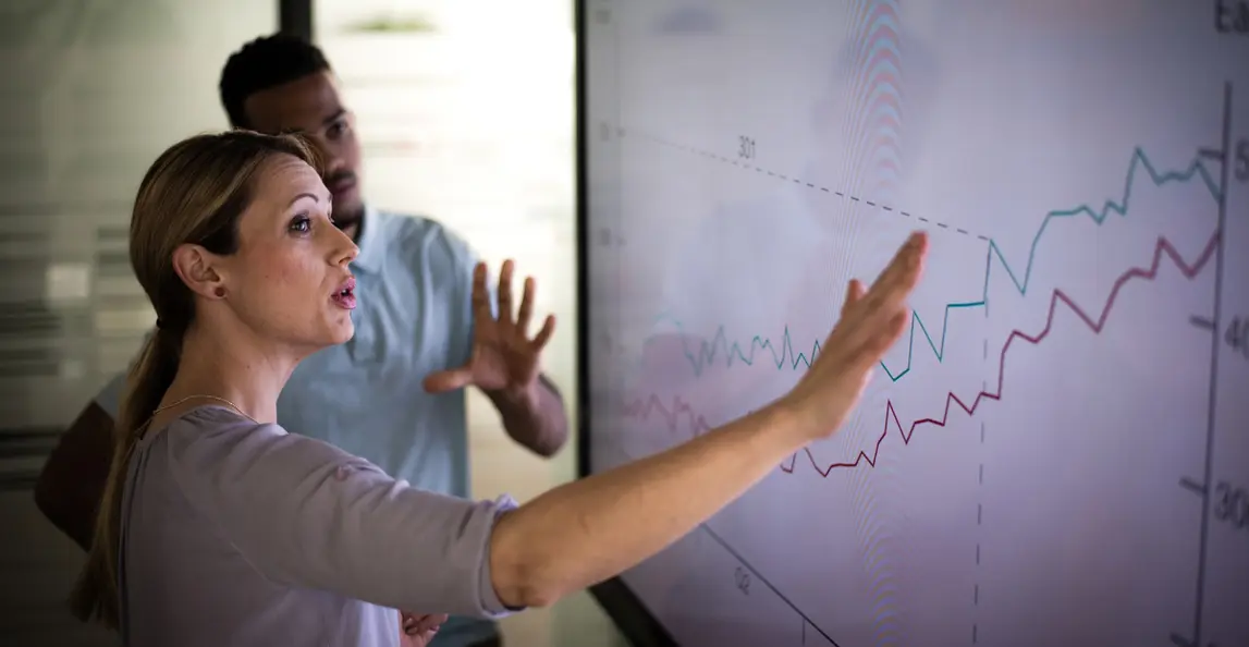 Two project managers analyzing performance data on a large display for project control