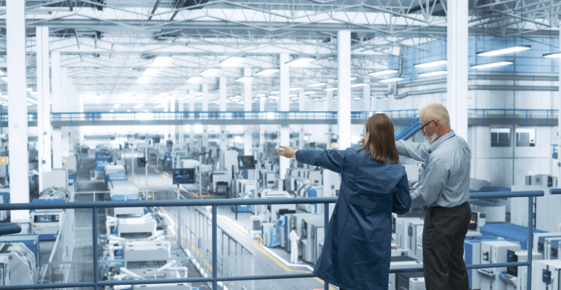 Two engineers overlooking a modern factory floor from an elevated platform