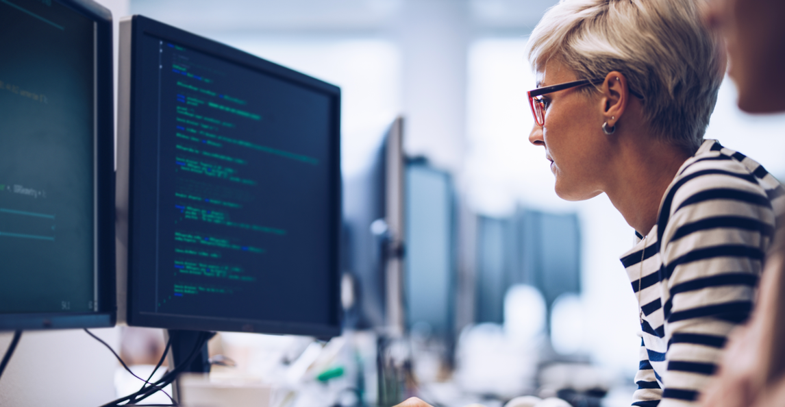 A female developer works on software at her desktop in a bright open-plan office.