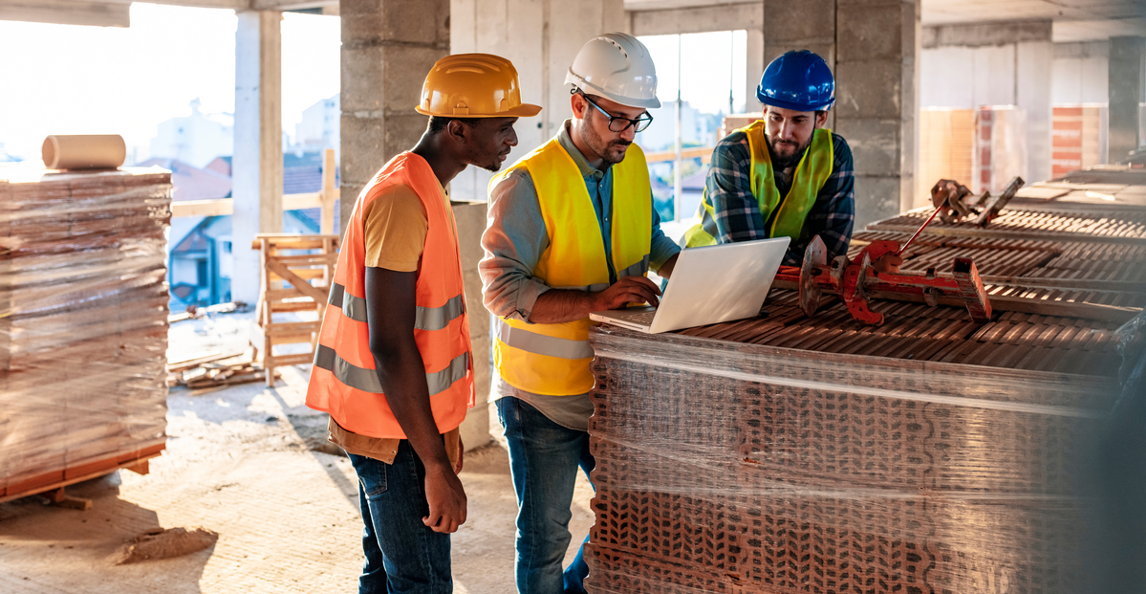Three construction workers reviewing project plans on a laptop at a job site