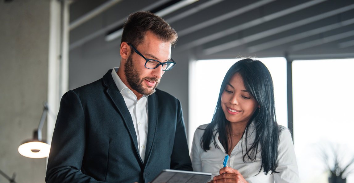Two business professionals reviewing data on a tablet in a modern office