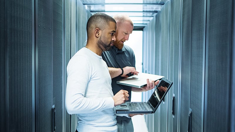 Two server room technicians working on laptops