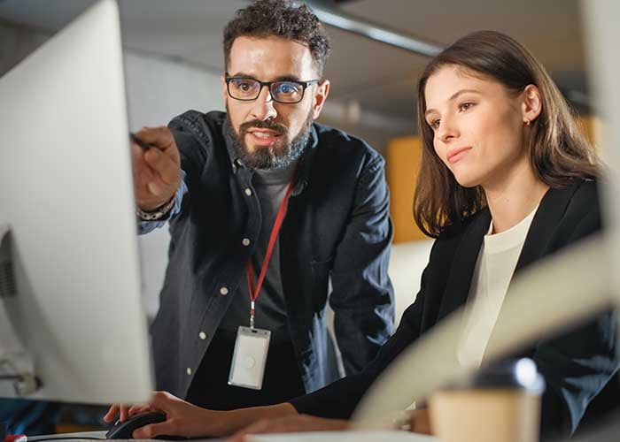Two employees collaborating at a computer in an office, discussing shift planning under a 2-2-3 work schedule