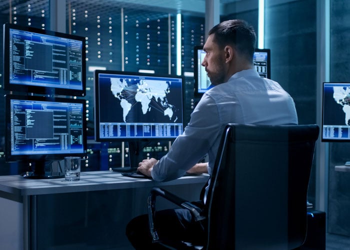 Analyst working in a server room with multiple monitors