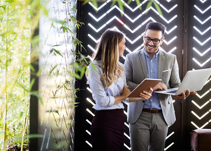 Business people standing up talking with a laptop and notepad 