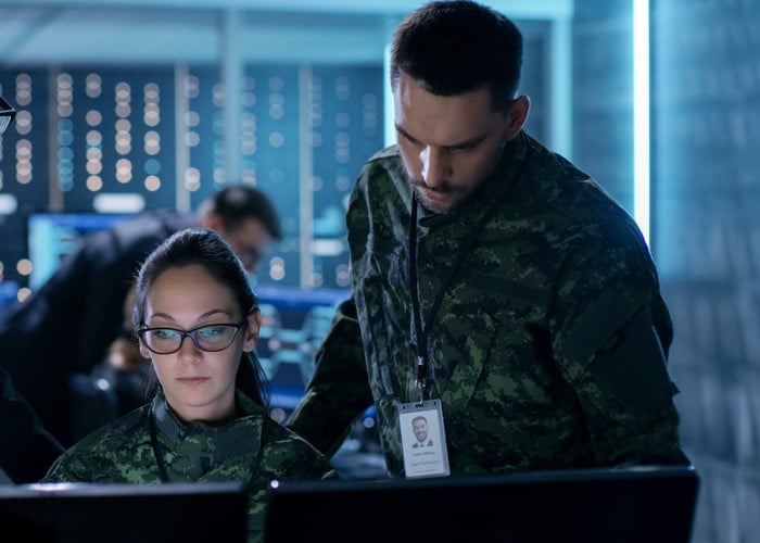 Team monitoring cybersecurity systems in military command center with advanced digital screens and data analytics