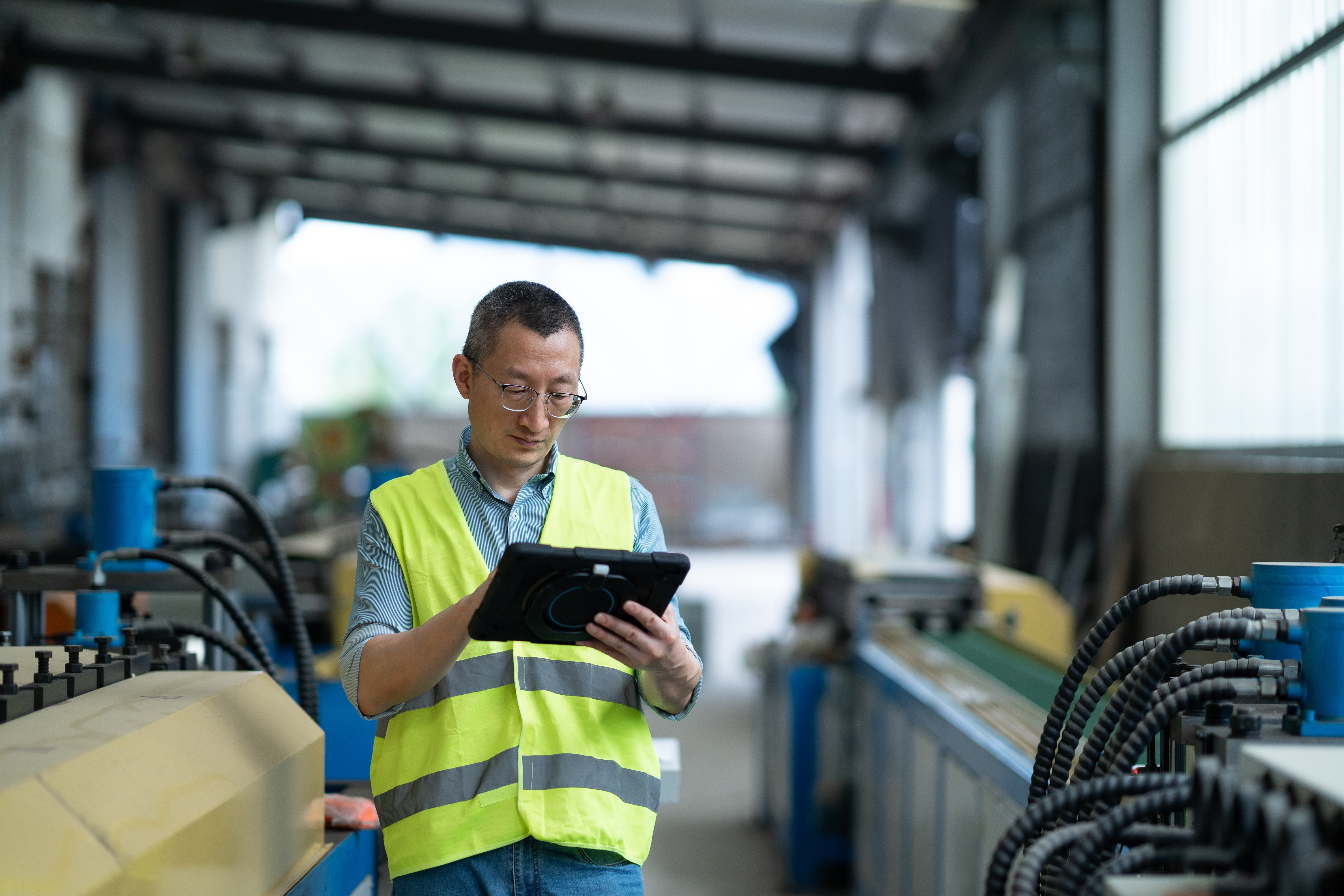 Industrial Operations Supervisor Monitoring Production Workflow and Data on Tablet in Manufacturing Facility