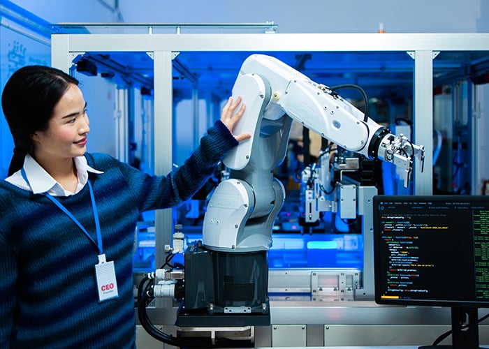 Woman operating a robotic arm beside a computer monitor