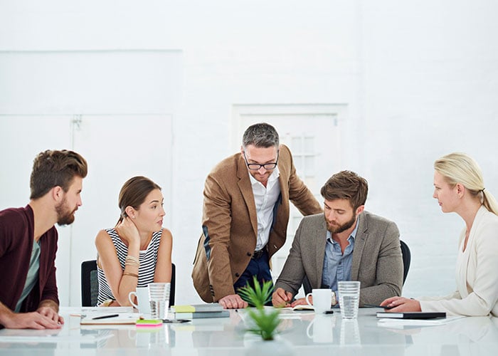 Five colleagues gathered around a table while one team member leads a discussion during a project meeting