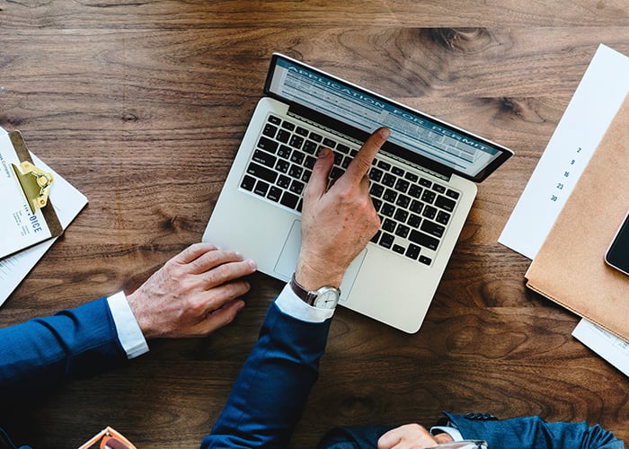 Business Professional Completing Permit Application and Compliance Documentation on Laptop