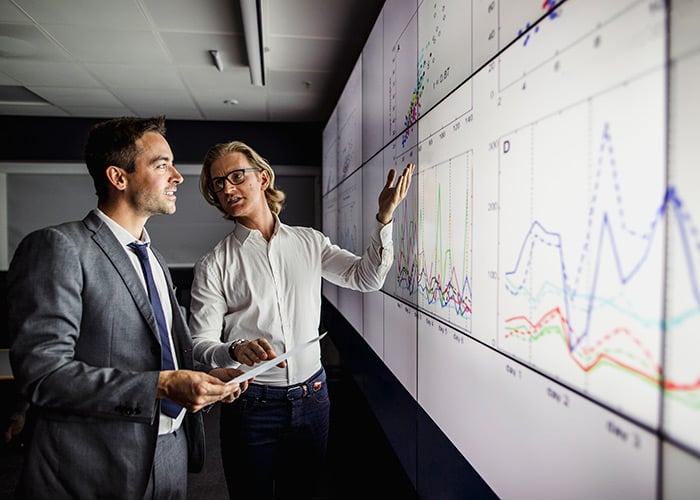 Business professionals in a dark room standing in front of a large data display screen with information