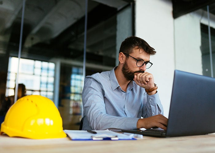 Construction Project Manager Reviewing Project Data and Reports on Laptop at Job Site Office